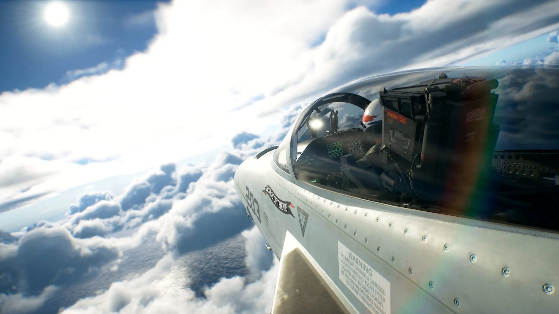 Still oficial de prensa de Ace Combat 8: Wings of Theve — caza gris marcado 203 y Wings of Theve, cabina sobre nubes soleadas y océano.