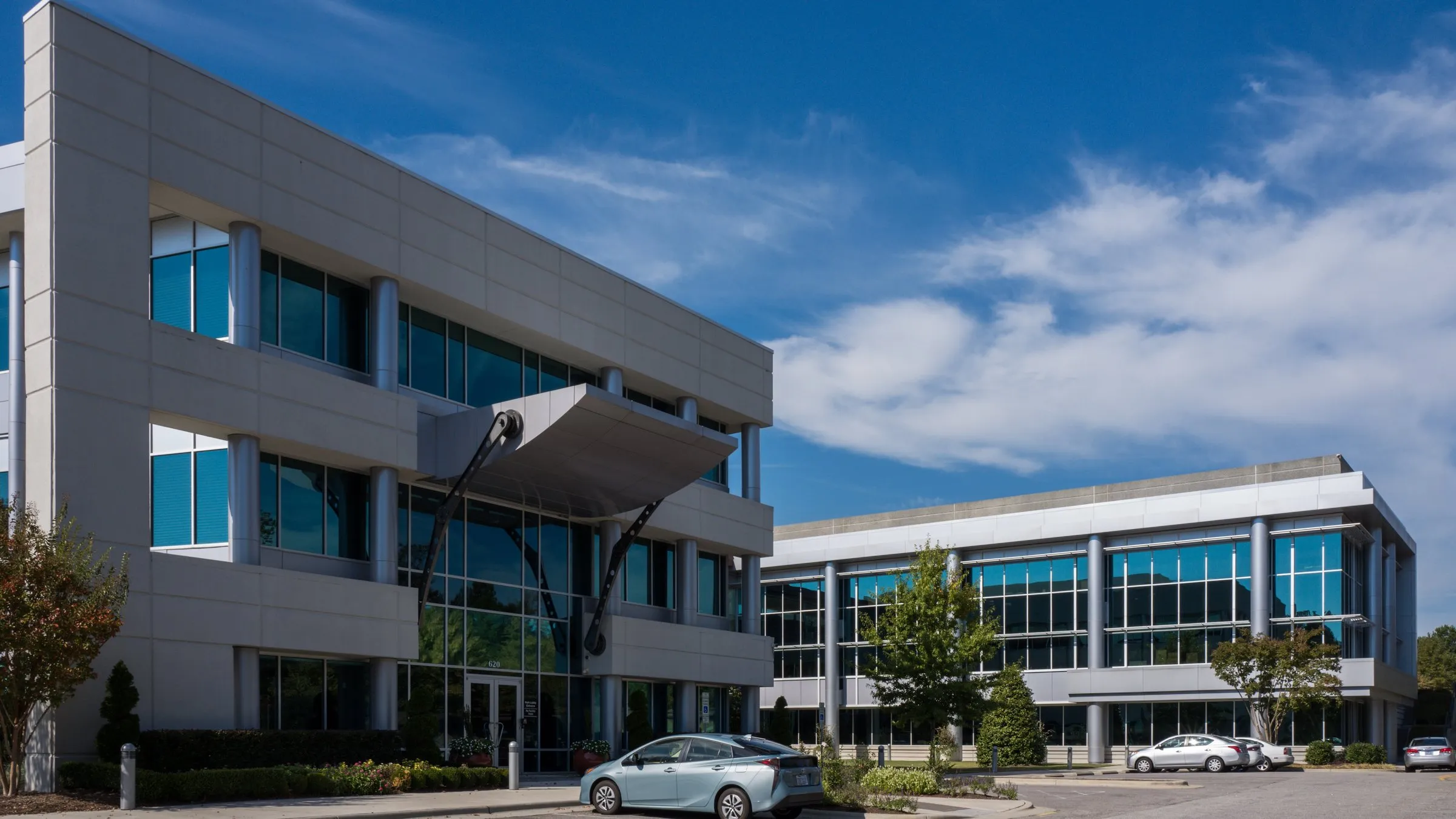 Epic Games' office buildings in Cary, North Carolina: two three-story glass-and-concrete buildings under a blue sky with scattered clouds, with cars in the parking lot.