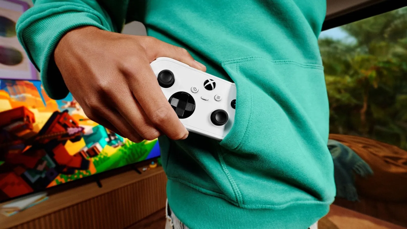 Illustrative Xbox promotional photo, not from the survey: a hand slips a white Xbox wireless controller into the pocket of a teal hoodie, with a game on a TV in the background.